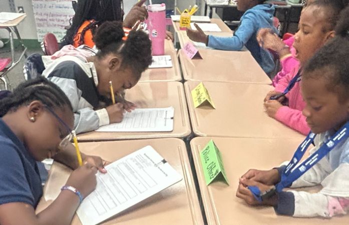  students sitting in desks talking and writing